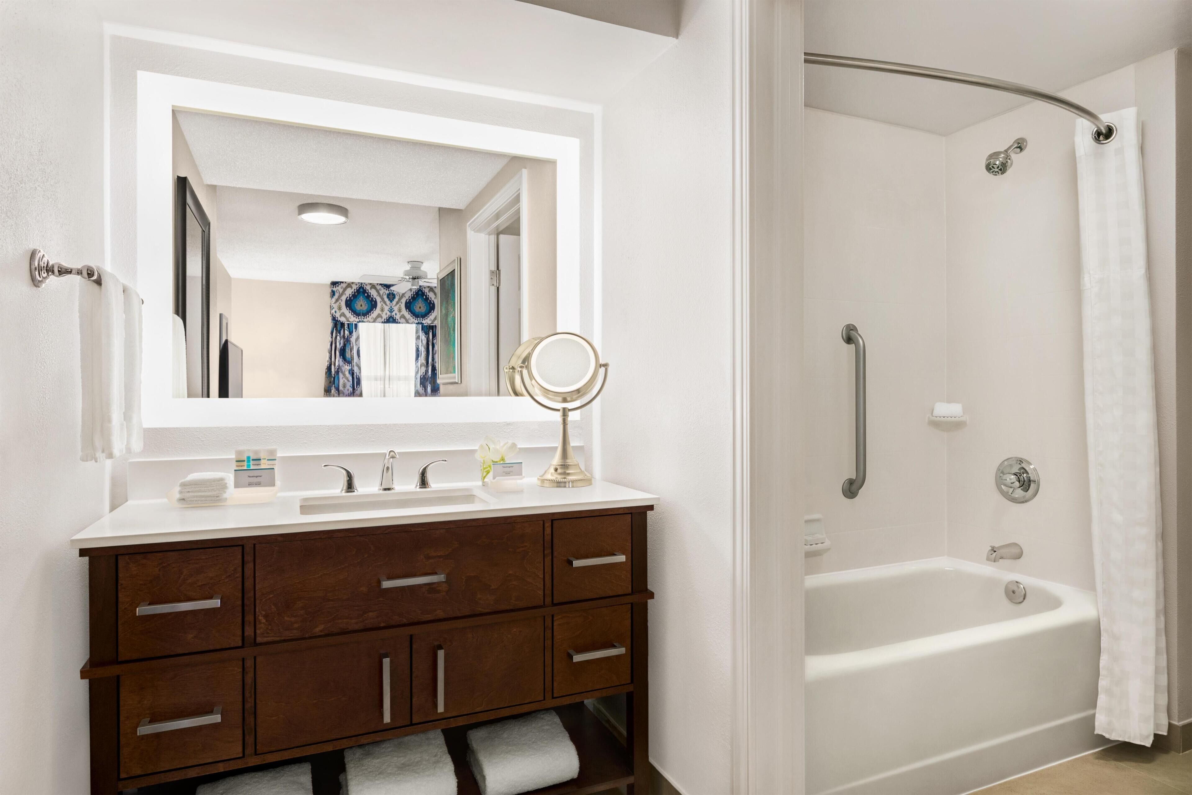 A bathroom with a white vanity, a large mirror, a bathtub, and a shower curtain.