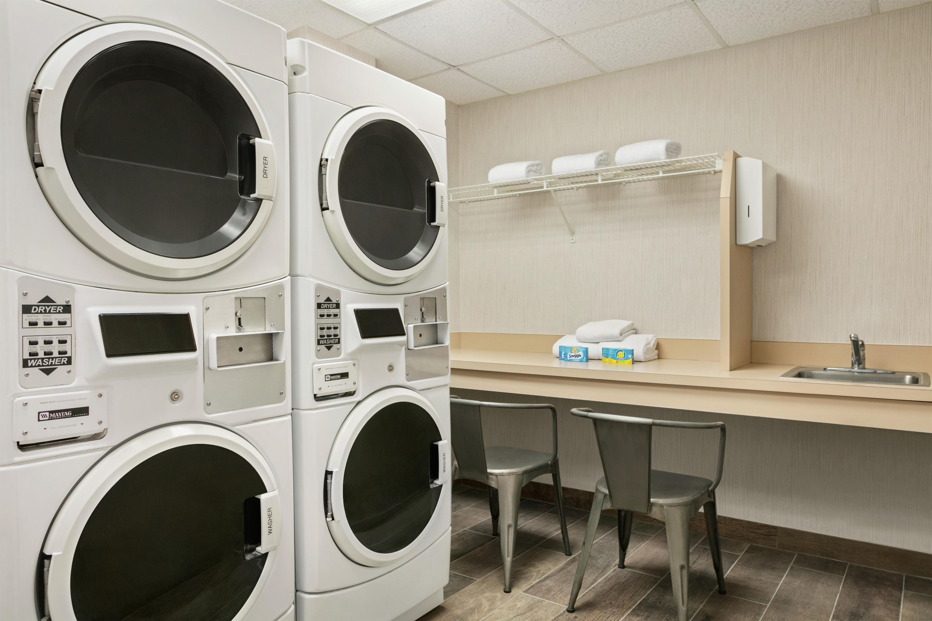A laundry facility with multiple washing machines, a sink, and two chairs.