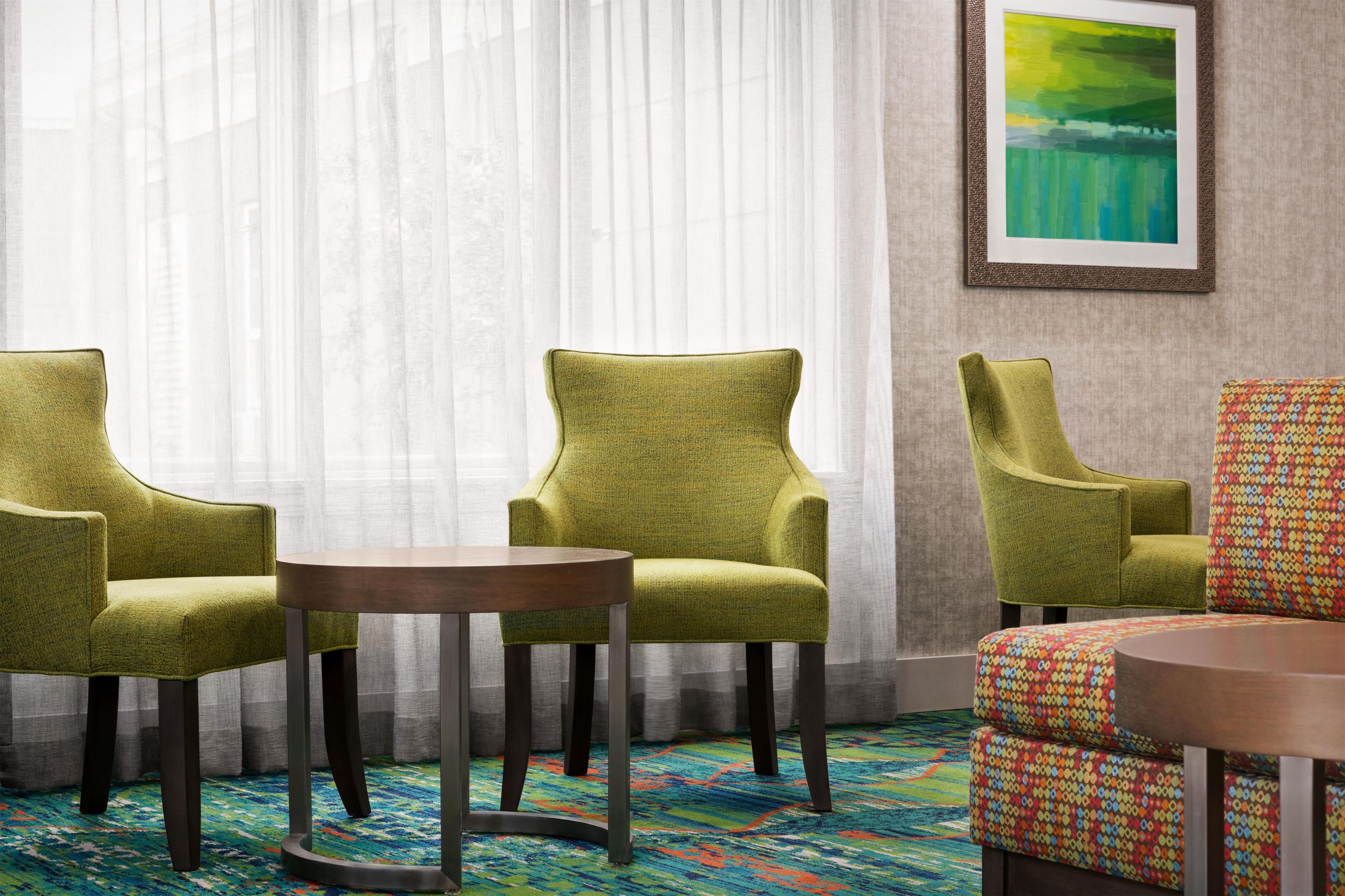 A hotel room with a green armchair, a round table, and a colorful sofa set.