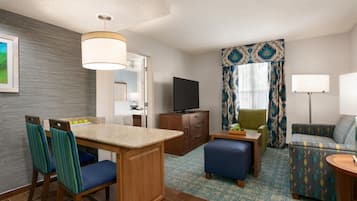 A hotel room with a kitchenette, a television, a sofa, and a dining area with chairs.