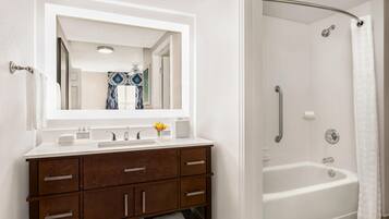 A bathroom with a white vanity, a large mirror, a bathtub, and a shower curtain.
