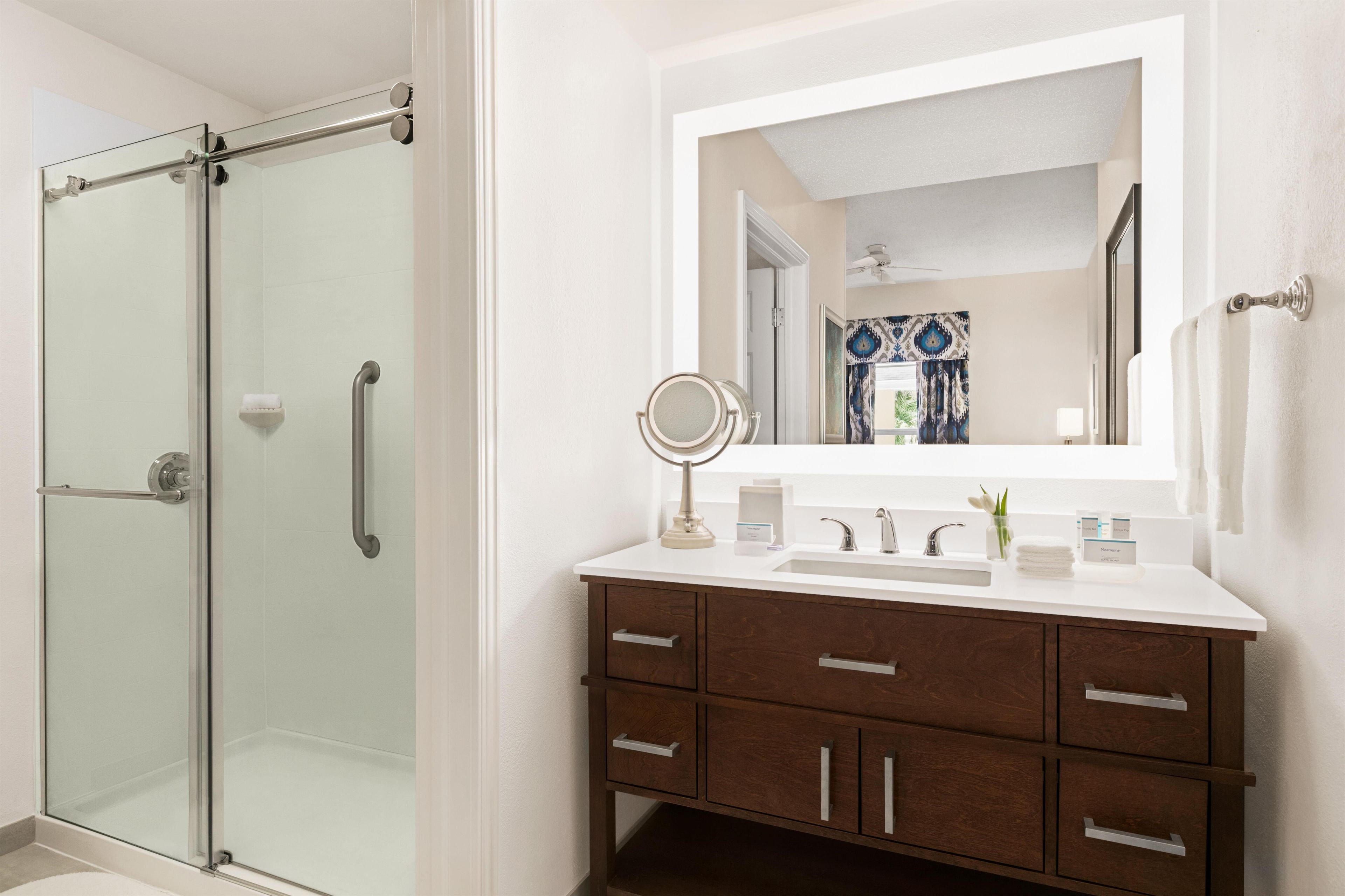 Un baño con cabina de ducha de vidrio, un lavabo blanco con espejo y un mueble de tocador de madera con cajones.