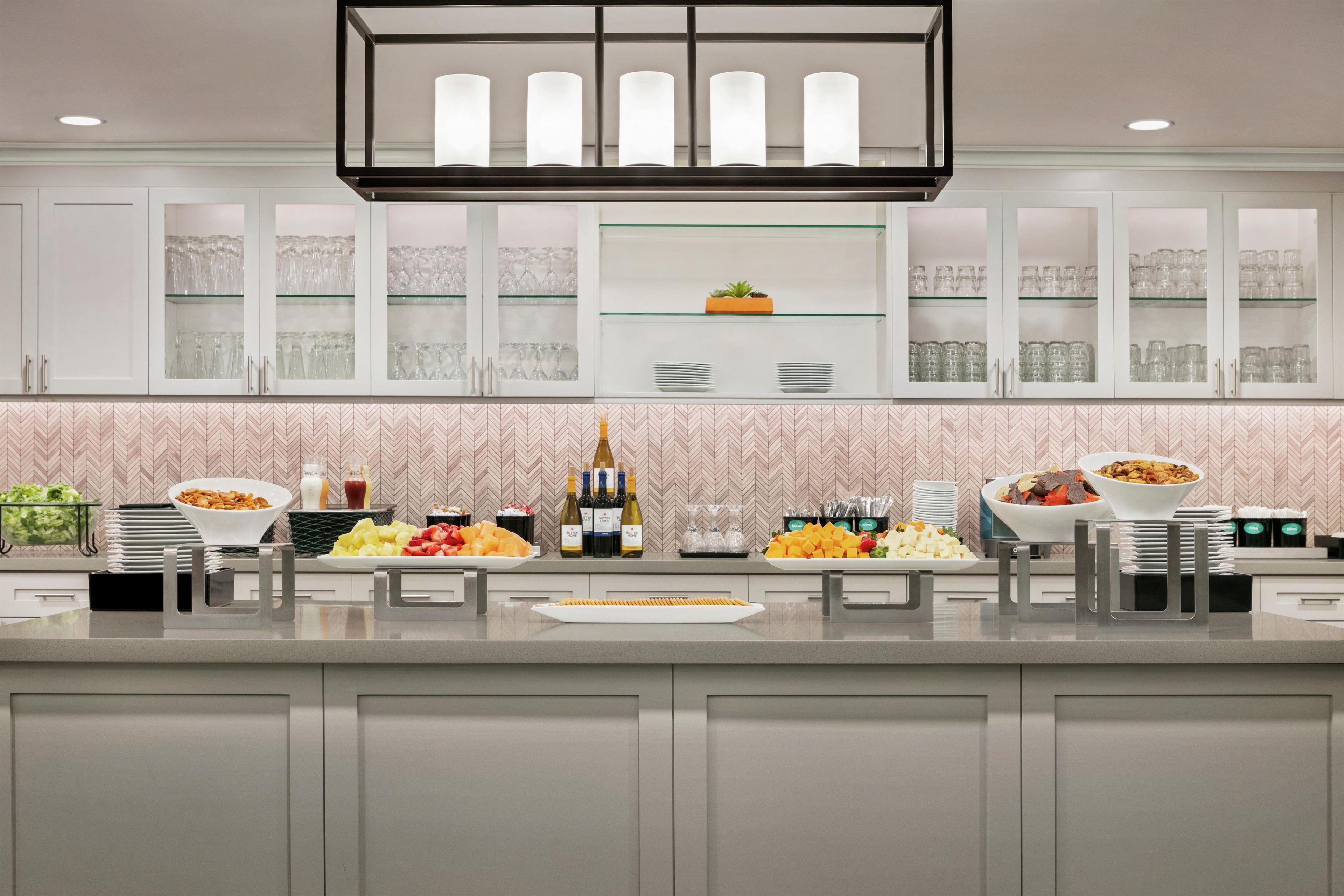 A modern kitchen with white cabinets, a glass display shelf, and various food items.