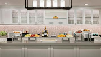 A modern kitchen with white cabinets, a glass display shelf, and various food items.