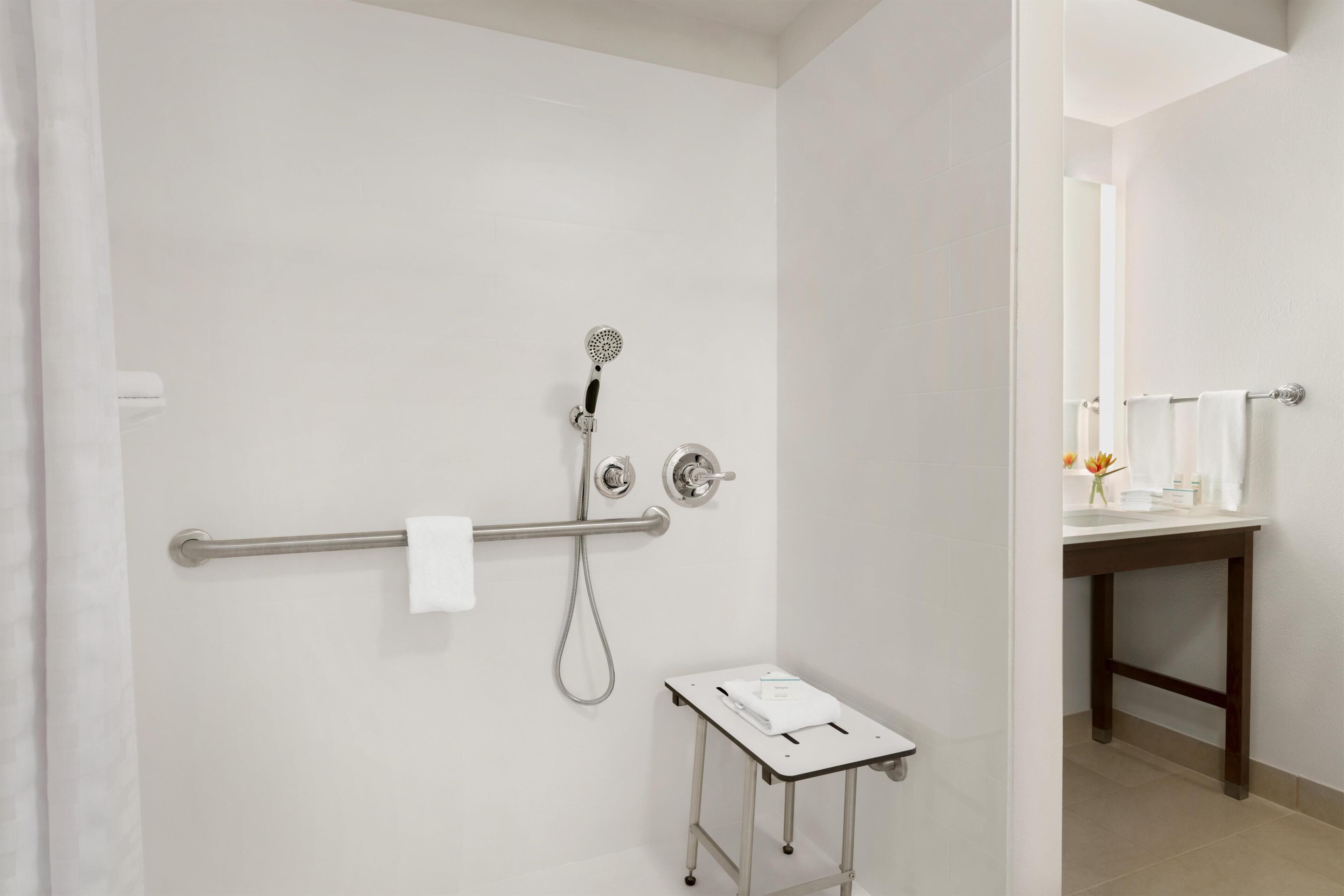Un baño moderno con ducha, barra de apoyo, una mesita y un espejo.