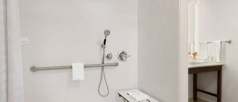 A modern bathroom with a shower, a handrail, a small table, and a mirror.