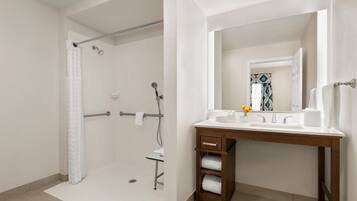 Un baño con ducha, lavabo con espejo y un perchero para toallas.