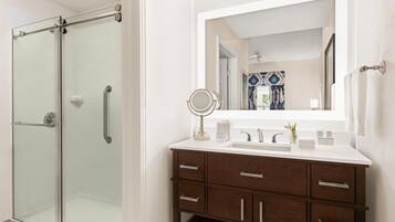 Un baño con cabina de ducha de vidrio, un lavabo blanco con espejo y un mueble de tocador de madera con cajones.