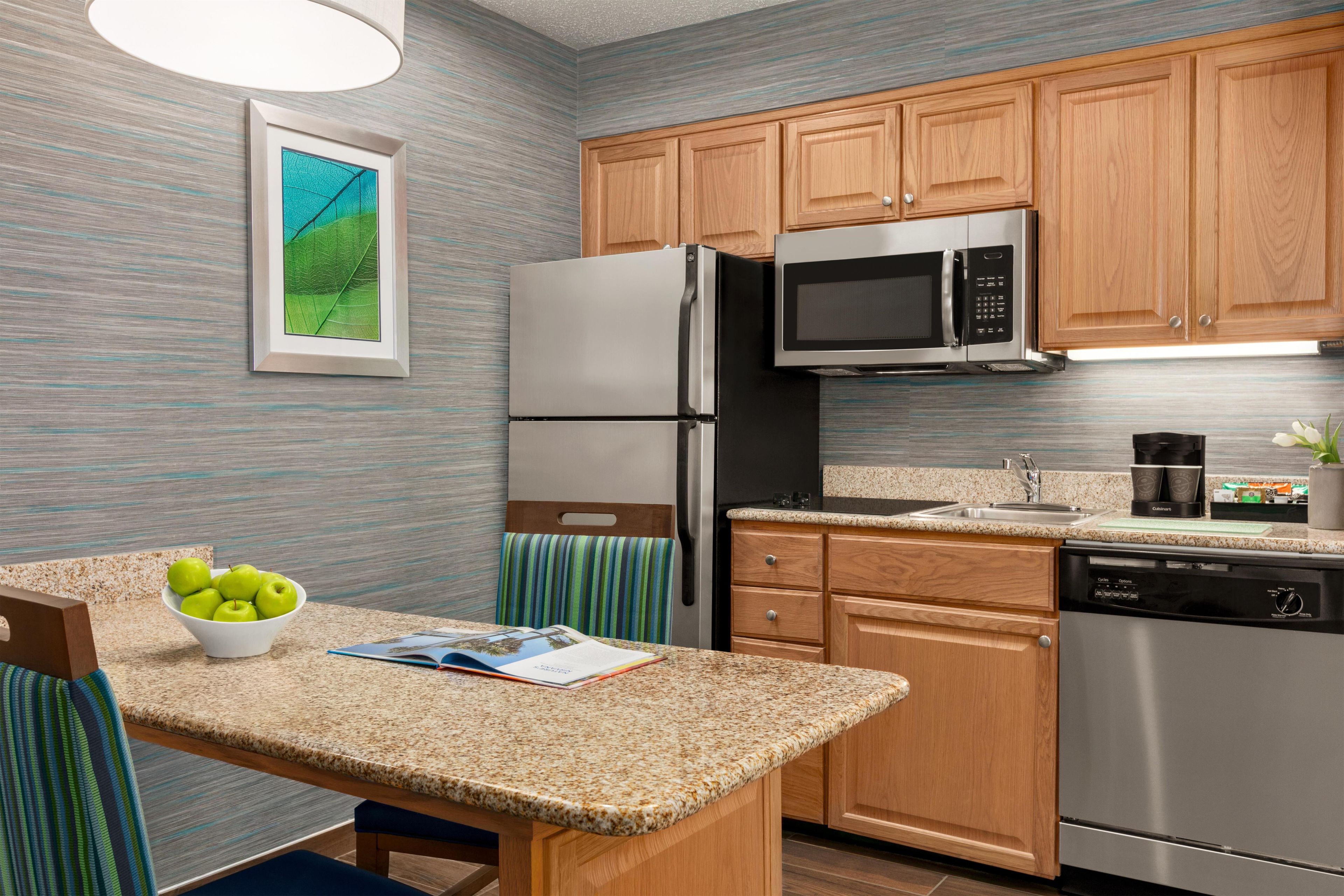 A kitchen with wooden cabinets, stainless steel appliances, a granite countertop, and a framed picture on the wall.