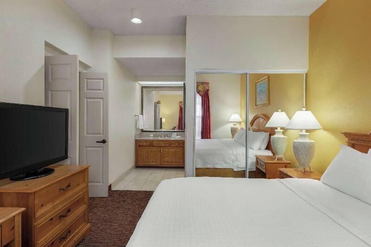 A hotel room with a bed, a television, a dresser, a mirror, and a bathroom visible through an open door.