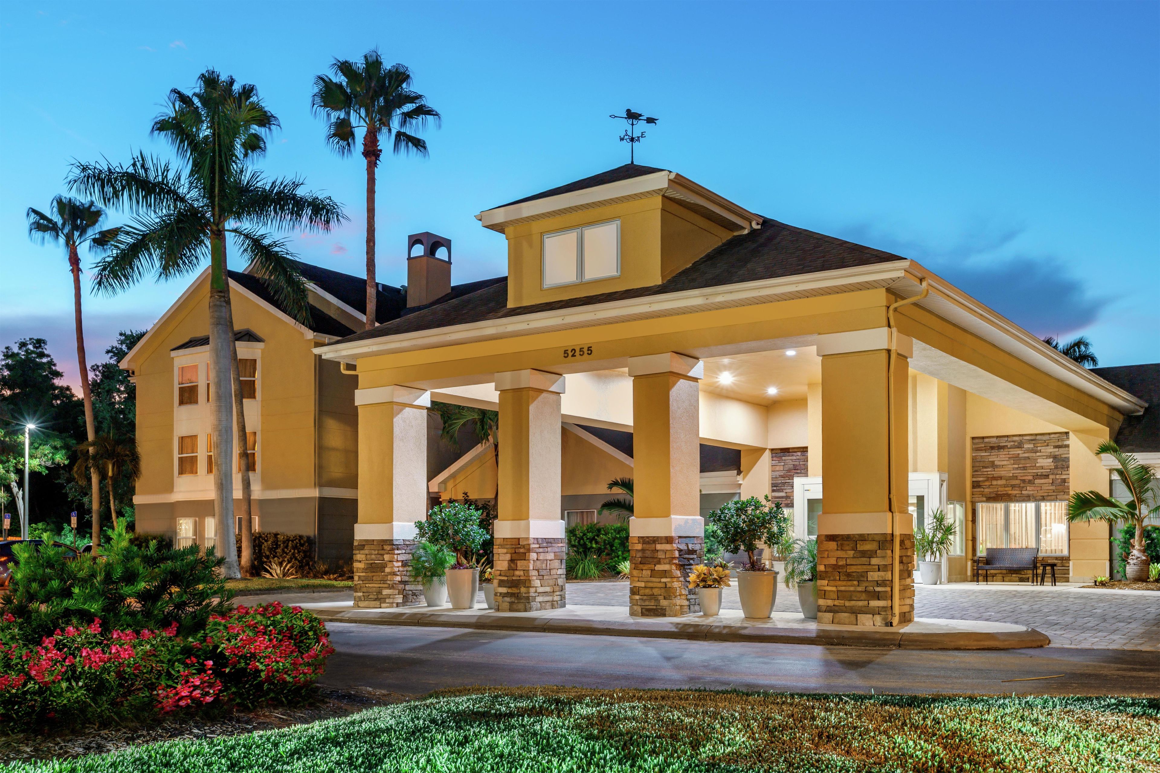 A hotel with a covered entrance, palm trees, and a well-maintained garden.