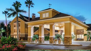 A hotel with a covered entrance, palm trees, and a well-maintained garden.