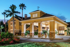 A hotel with a covered entrance, palm trees, and a well-maintained garden. - Homewood Suites by Hilton - Fort Myers (Fort Myers)