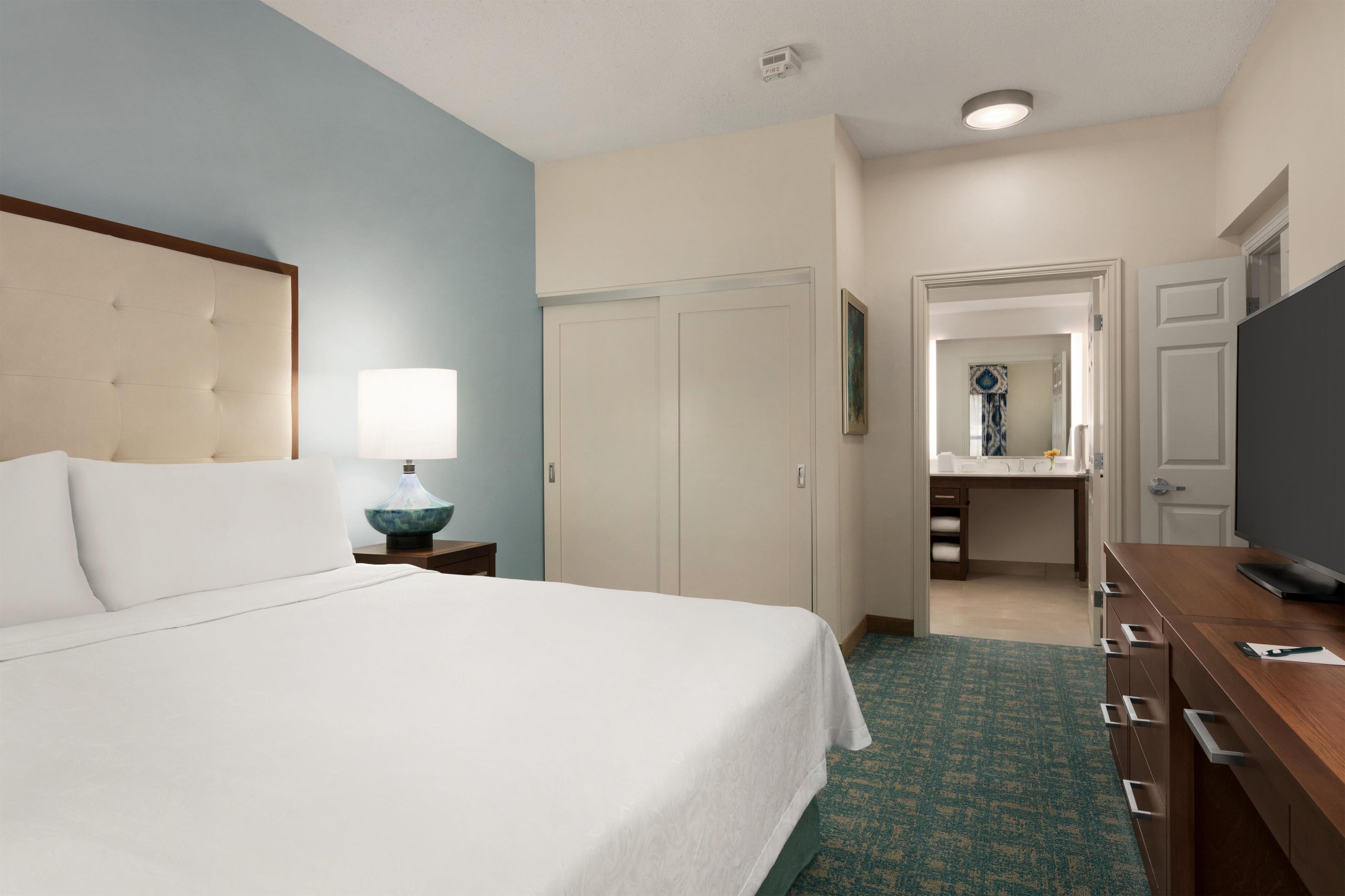 A hotel room with a bed, a desk, a mirror, and a television.