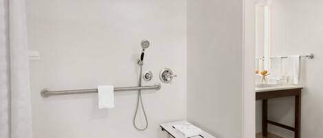 A modern bathroom with a shower, a handrail, a small table, and a mirror.