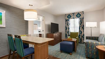 A hotel room with a kitchenette, a television, a sofa, and a dining area with chairs.
