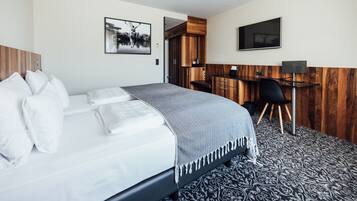 A modern hotel room with a neatly made bed, a desk with a chair, and a television on the wall.