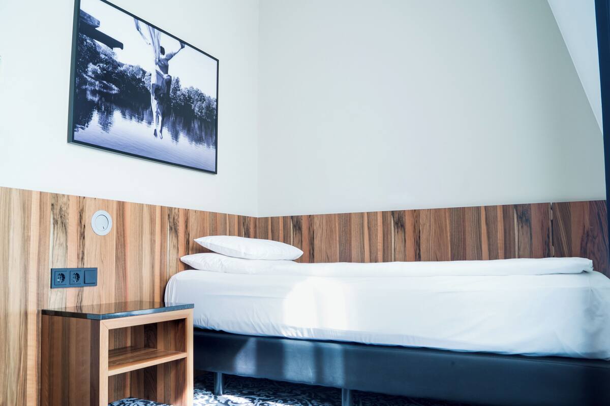 Un dormitorio con cama, cabecero de madera, mesita de noche y un cuadro colgado en la pared.