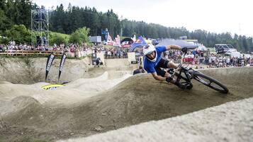 A dirt bike racer navigating a steep, sandy track with a crowd watching from the sidelines.