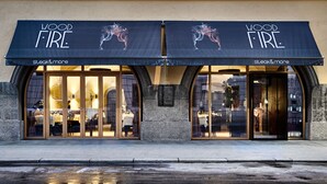 Ein Restaurant namens "Wood Fire" mit einer schwarzen Markise und Glasüren, das ein Logo mit einem Reiter und Pferd zeigt.