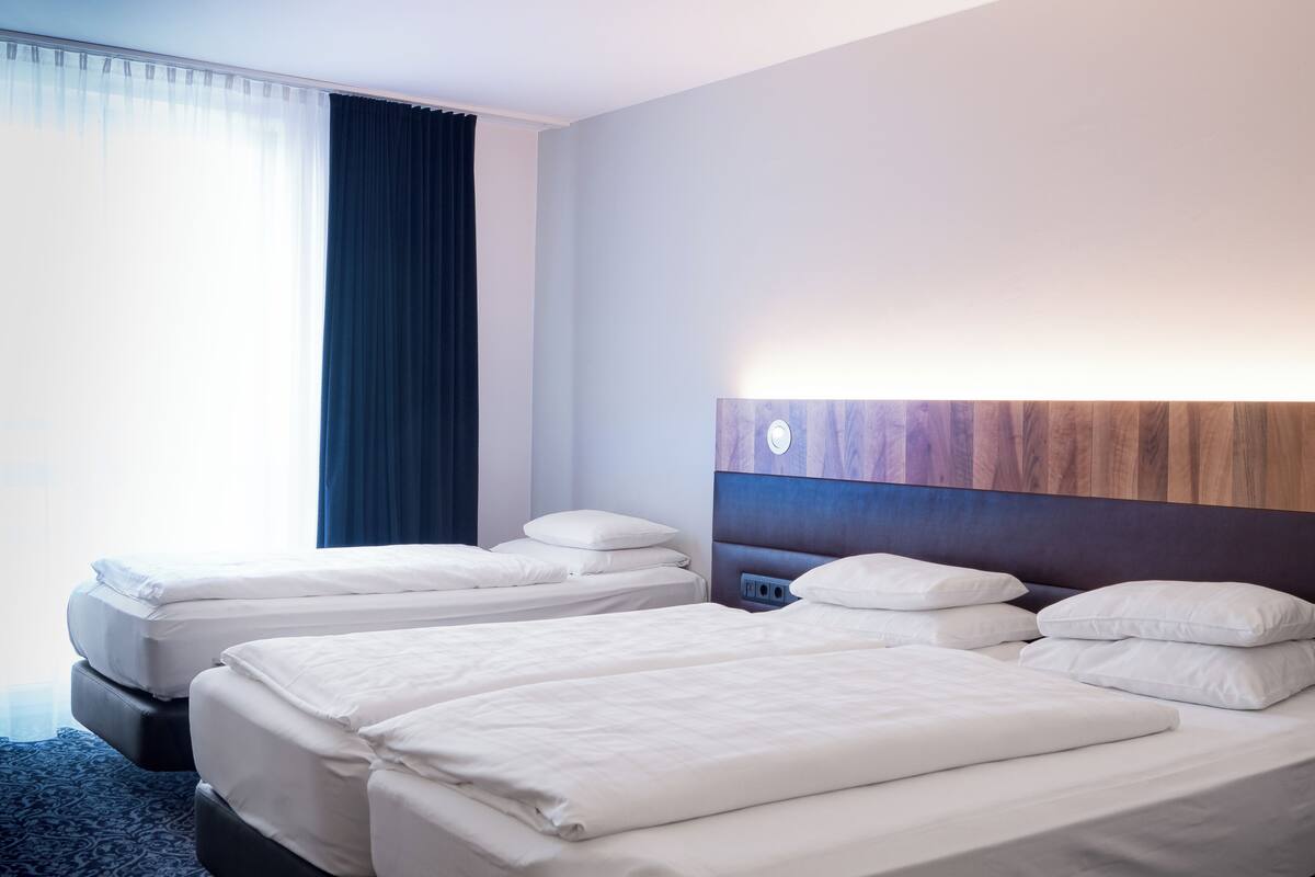 Una habitación de hotel con dos camas, cabecero de madera y un ventanal con cortinas.