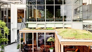 Ein modernes Gebäude mit einem Glasatrium, einer Außenbestuhlung und einem Dachgarten.