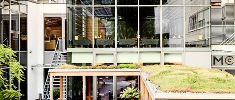 Un bâtiment moderne doté d’un atrium en verre, d’un espace extérieur aménagé pour s’asseoir et d’un jardin sur le toit.