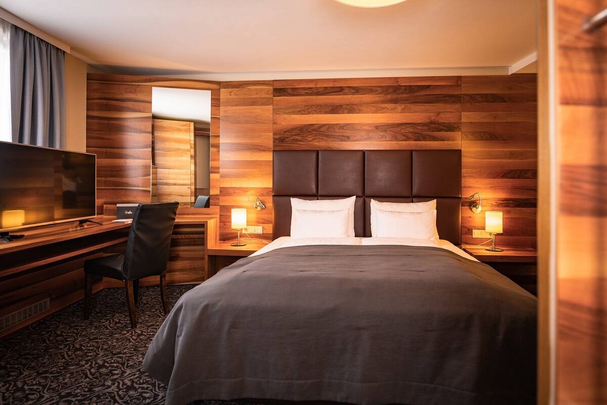 Una habitación de hotel con una cama grande, un televisor, un escritorio con una silla y dos lámparas de noche.