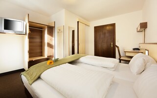 Habitación de hotel con cama, escritorio, silla, televisor y armario.