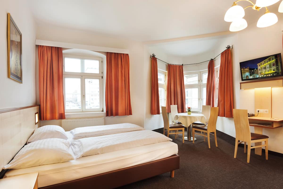 A hotel room with a bed, a desk, two chairs, a table, and a painting on the wall.