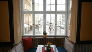 A room with a large window, a blue sofa, a small table with a vase of flowers, and striped patterned cushions. - Hotel Goldene Krone (Innsbruck)
