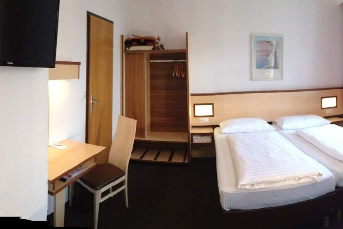 A hotel room with two beds, a desk, a chair, a TV, and a wardrobe.