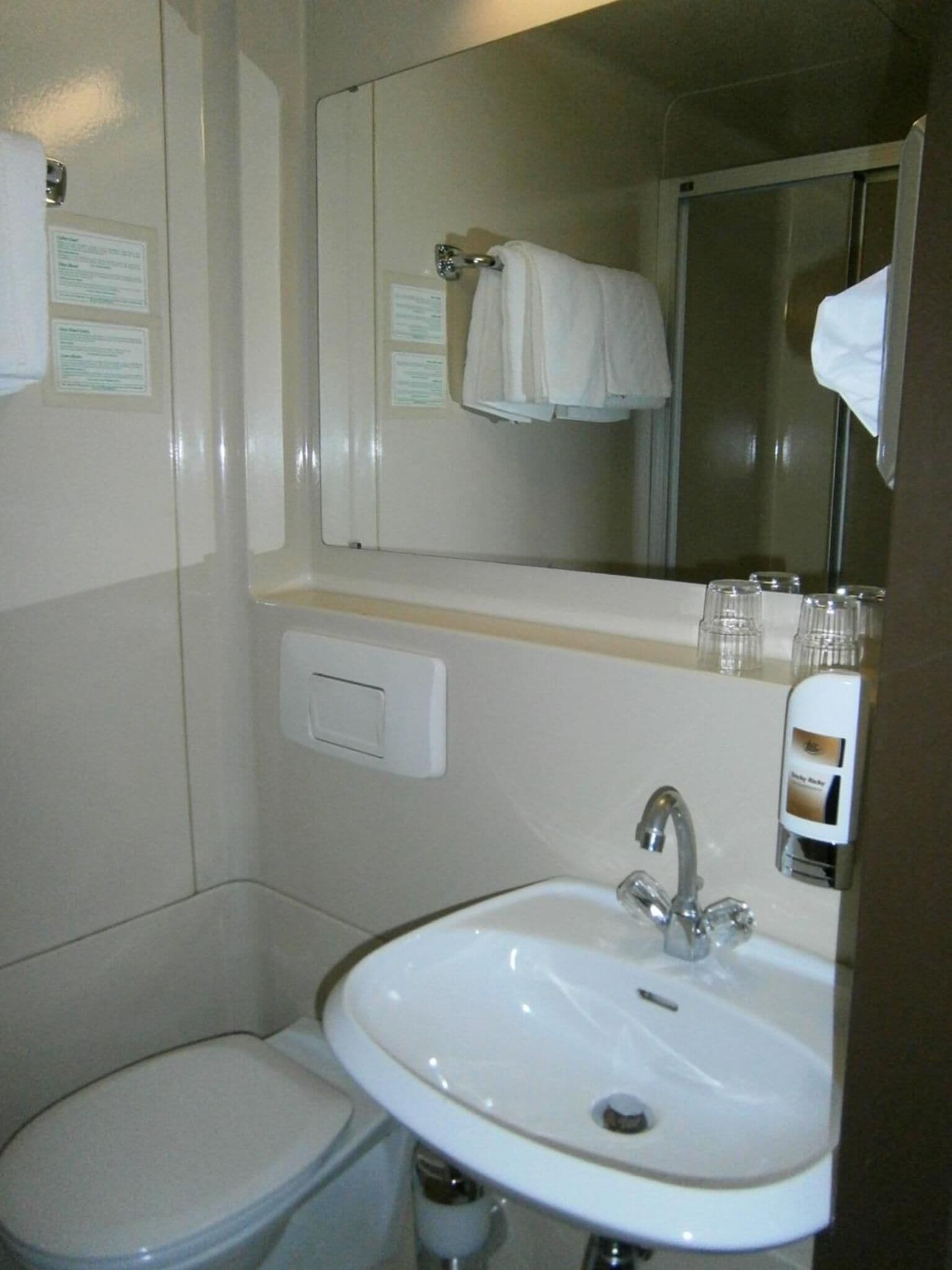 Une petite salle de bain avec des toilettes blanches, un lavabo surmonté d’un miroir et une serviette accrochée au mur.