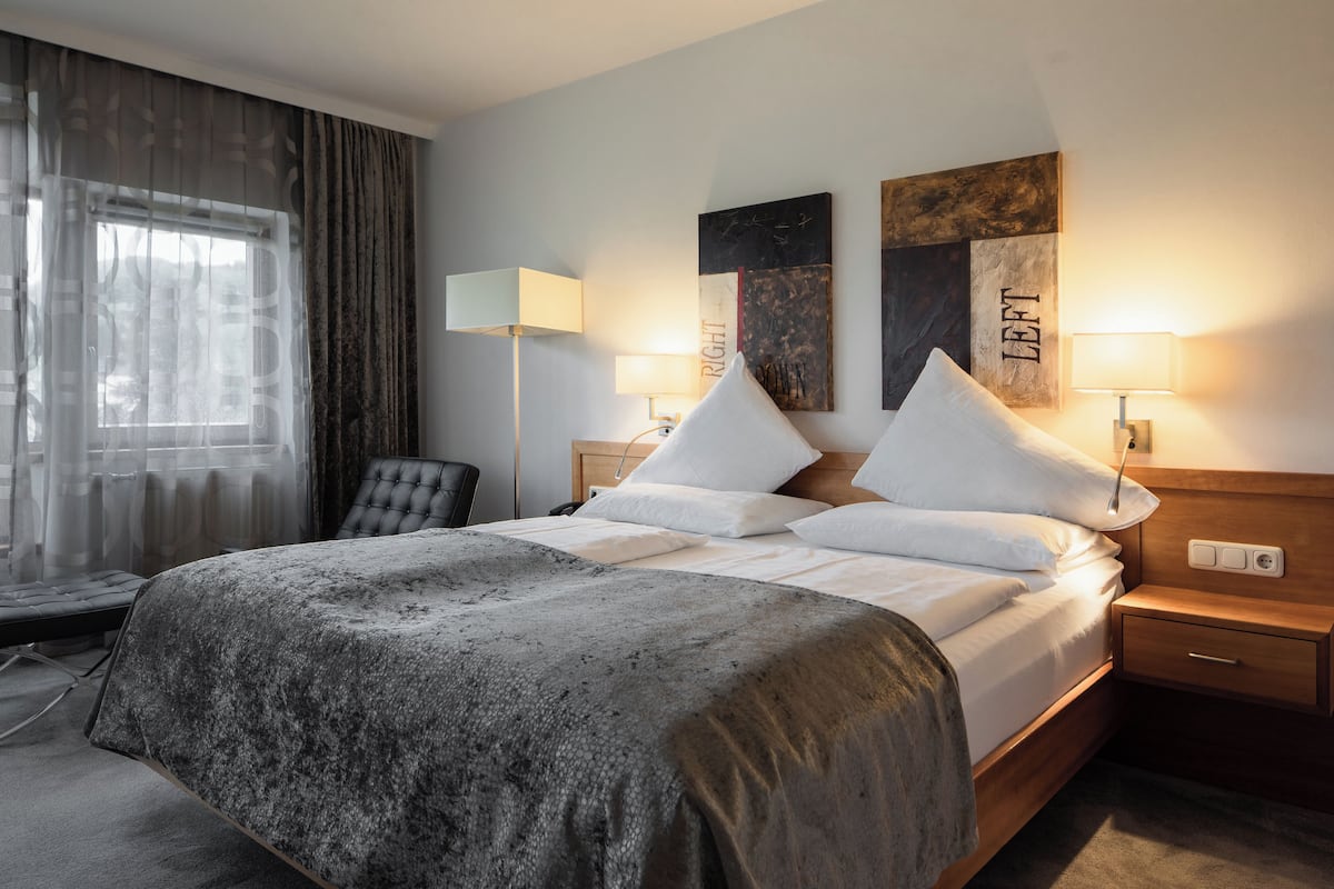 A neatly made bed with a grey textured bedspread, two bedside lamps, a wooden headboard, and a wall with two framed artworks.