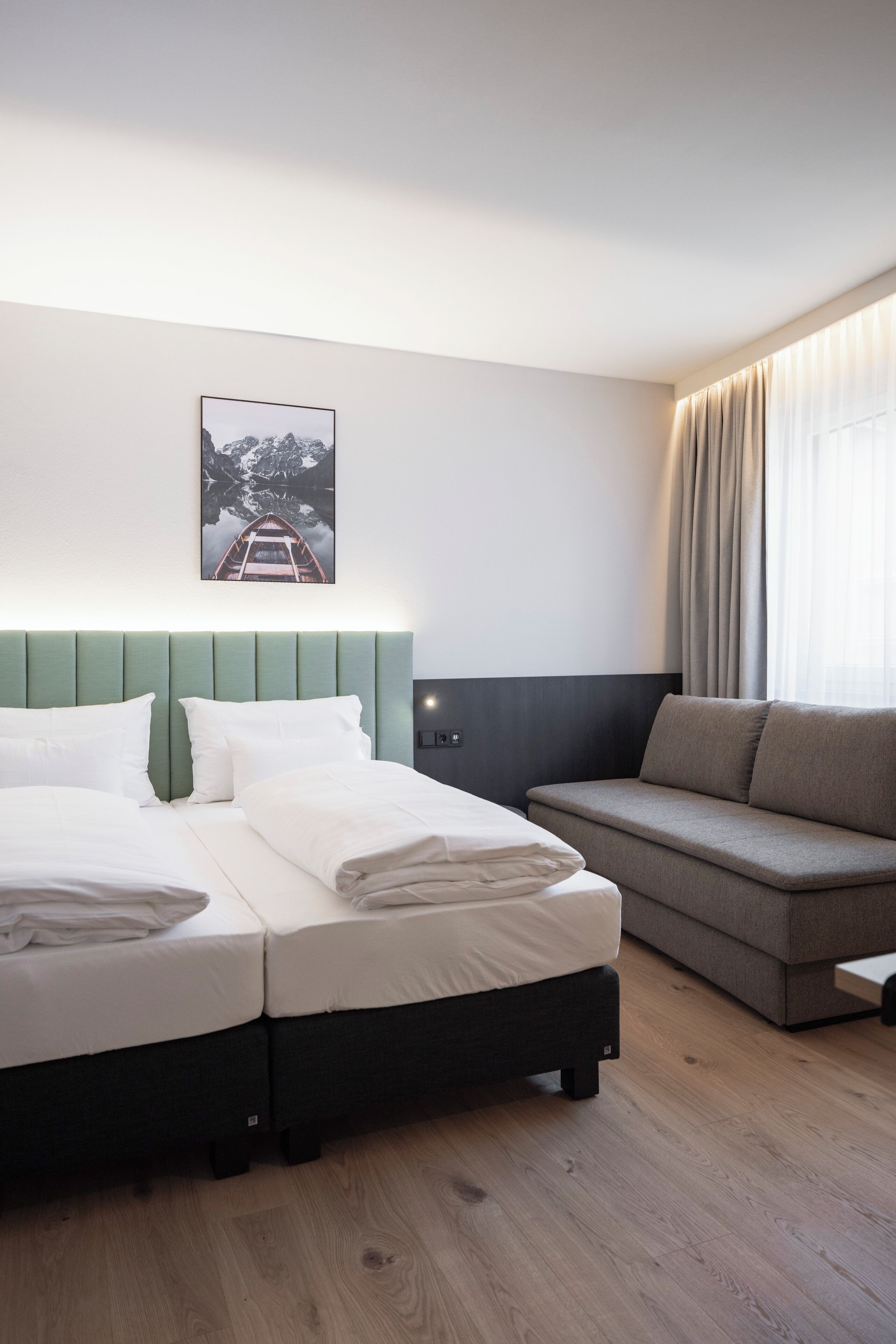 A hotel room with a bed, a sofa, a picture on the wall, and a window with curtains.