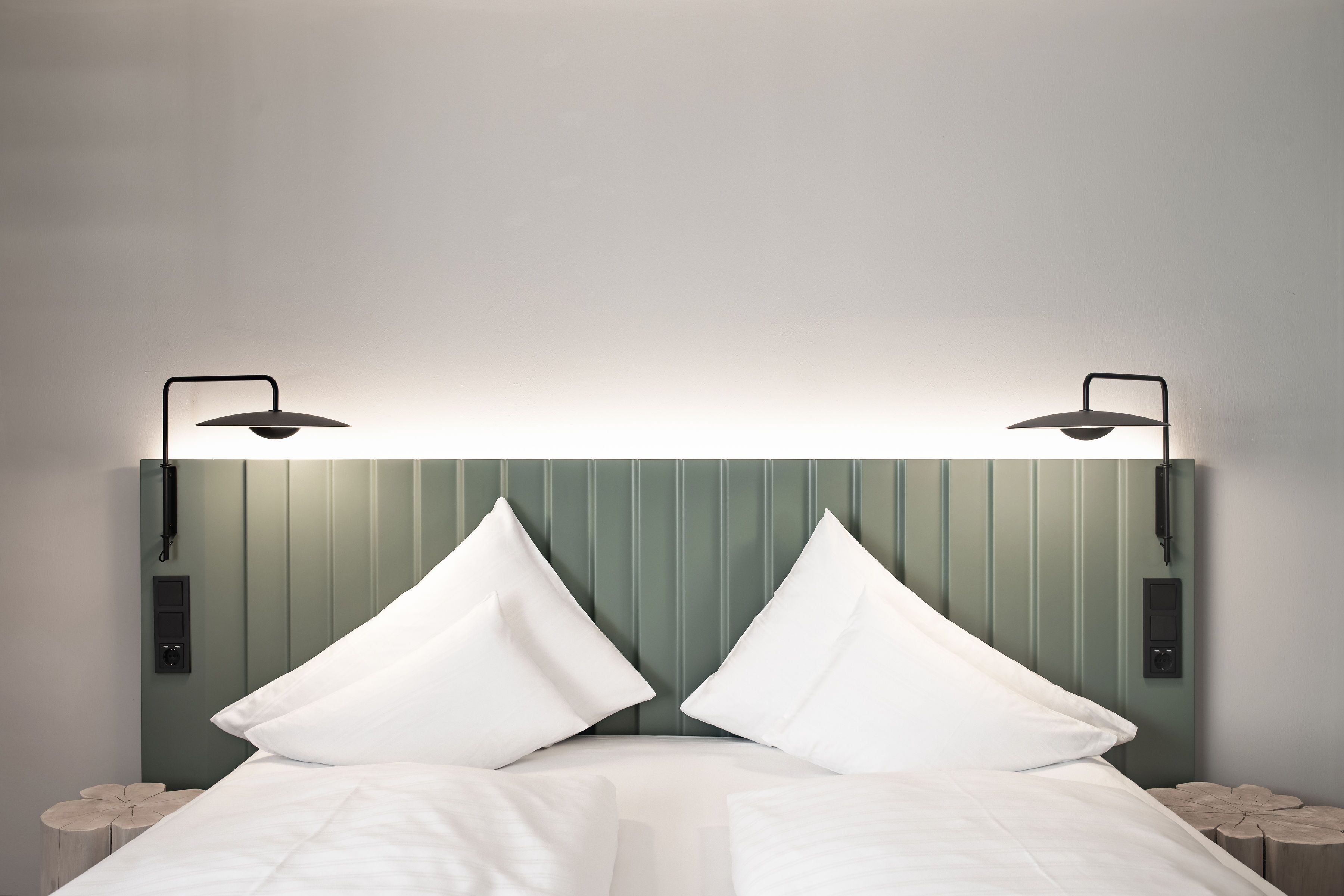 A bed with white linens and two pillows, flanked by two bedside tables with lamps.