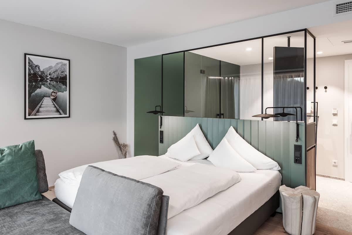 A modern hotel room with a large bed, a green accent wall, a mirror, and a framed picture of a mountain landscape.