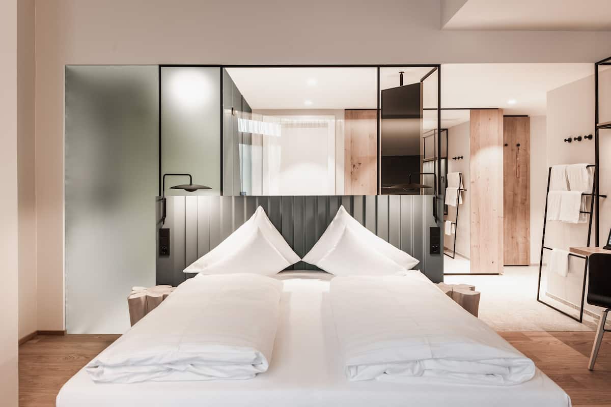 A modern hotel room with a large bed, a wooden wardrobe, and a mirror.