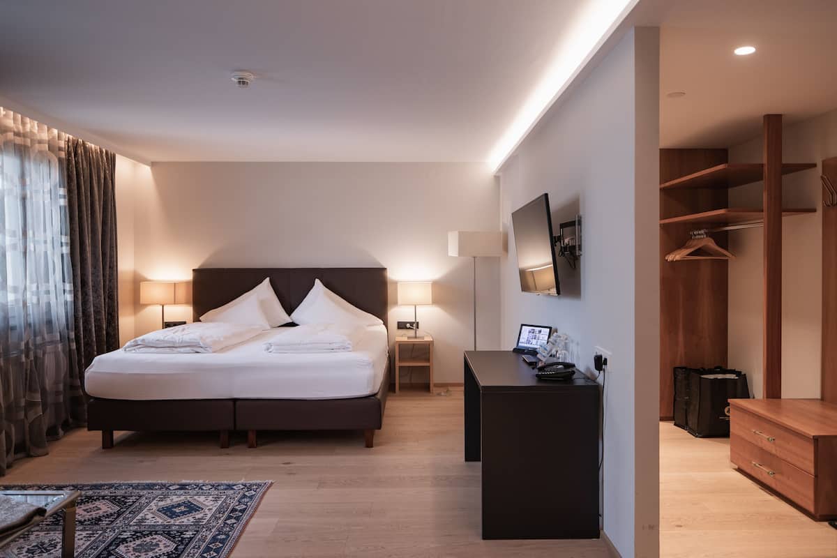A modern hotel room with a large bed, bedside lamps, a desk, a TV, and a wardrobe.