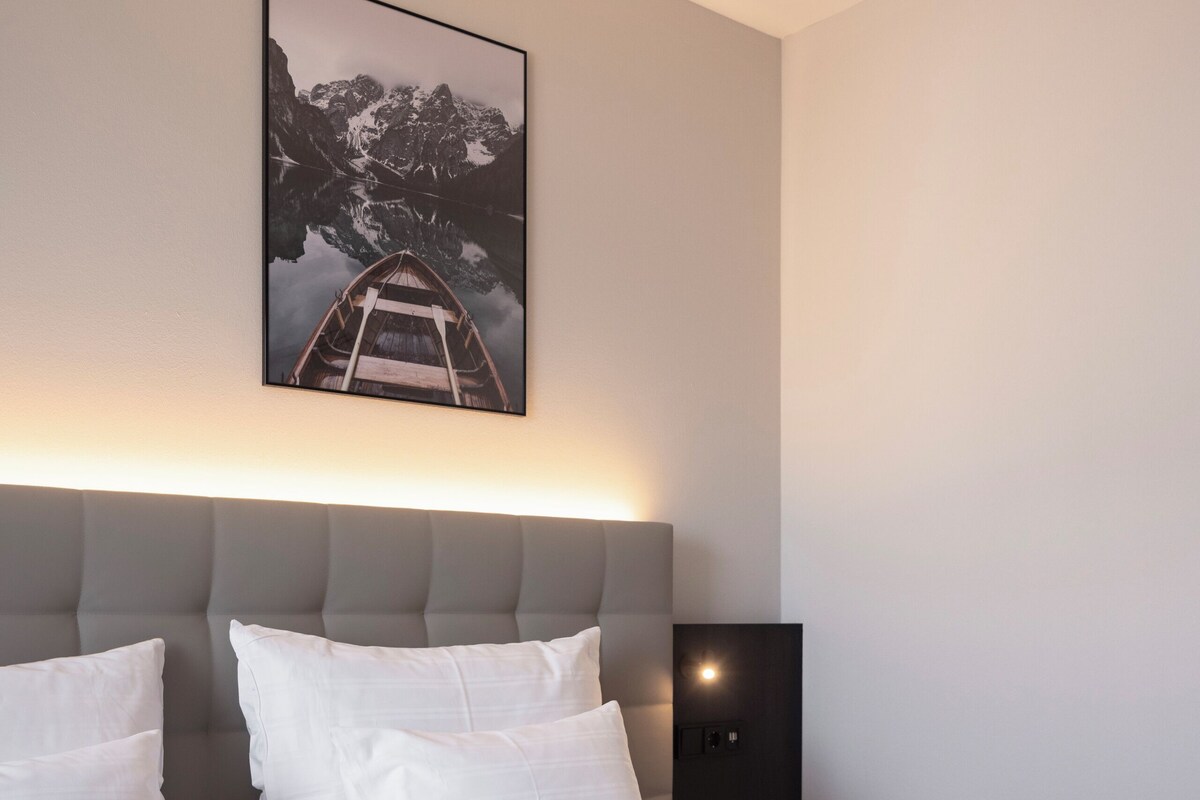 Une chambre d’hôtel moderne avec un grand lit, une tête de lit, une table de chevet et un tableau encadré au mur.