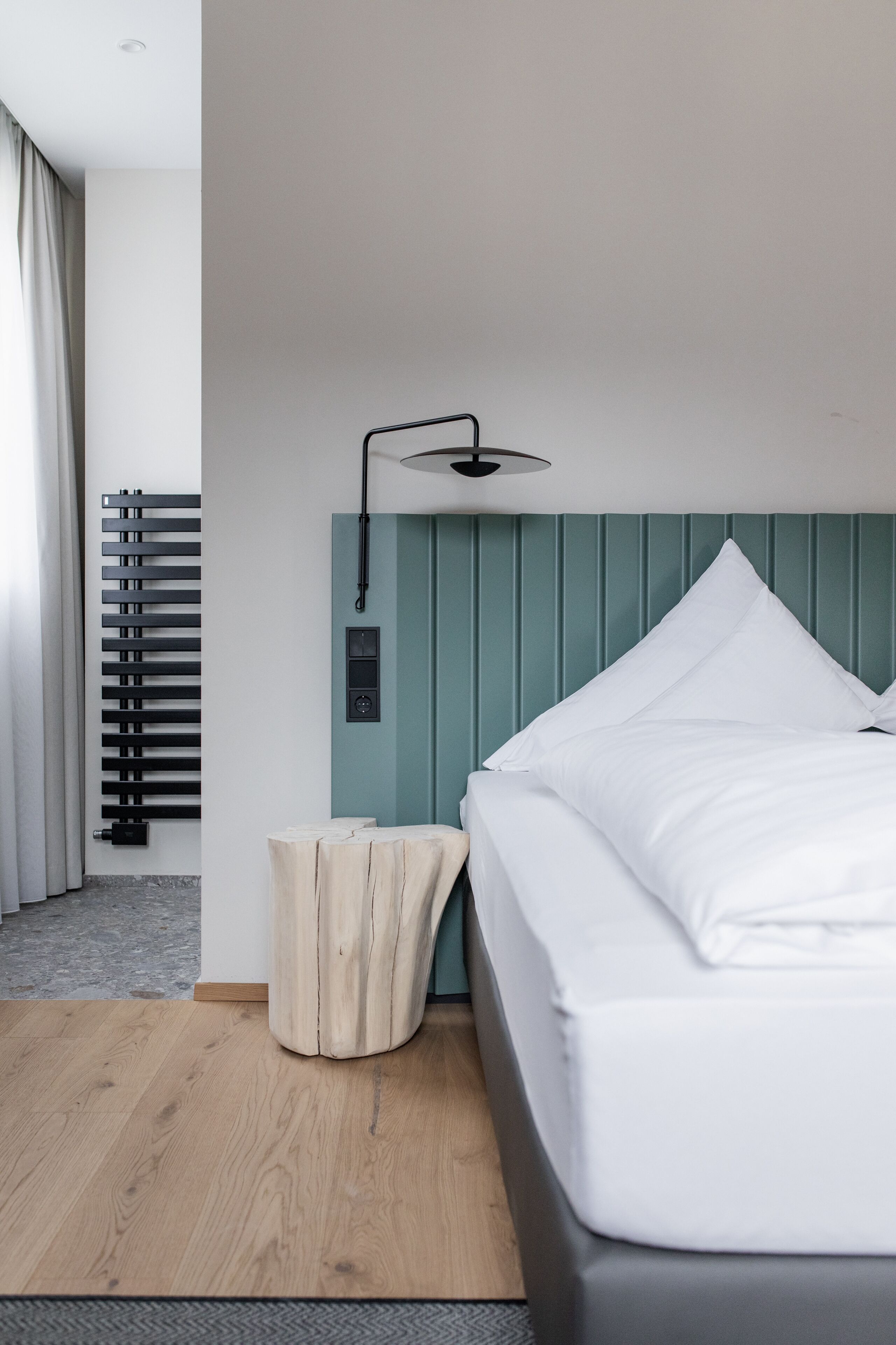 A modern hotel room with a bed, a bedside table, a lamp, and a radiator.