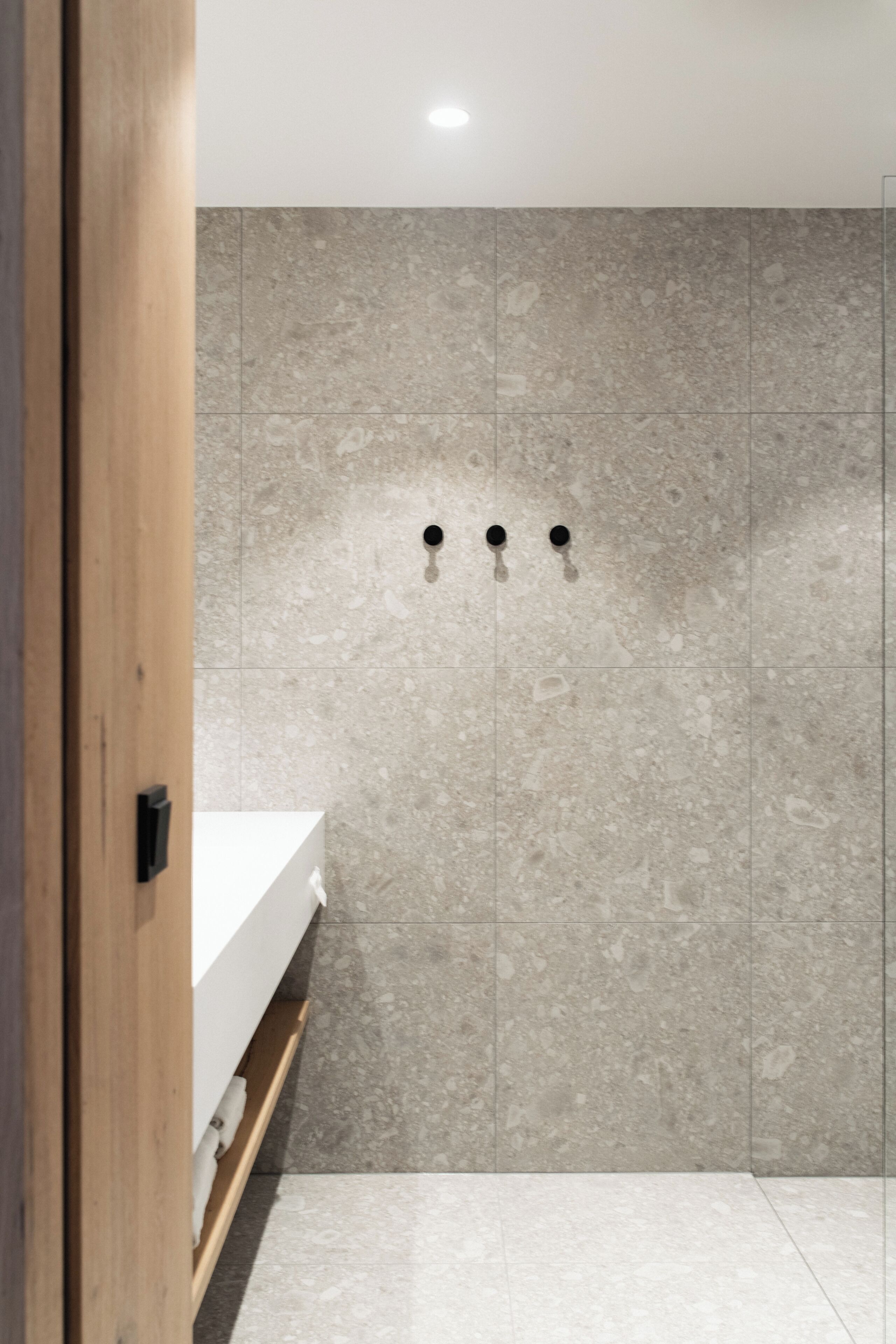 A bathroom with a wooden door, a white sink, and a tiled wall with three black fixtures.