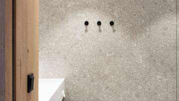 A bathroom with a wooden door, a white sink, and a tiled wall with three black fixtures.