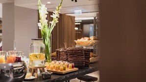 Un bufé de desayuno con diversas opciones de comida, una presentación de frutas y un jarrón con flores blancas.