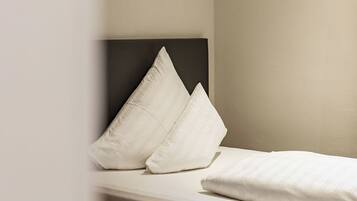 Una cama individual con cabecera oscura y dos almohadas en una habitación con paredes de tonos neutros.