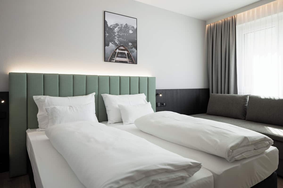 A hotel room with a bed, a sofa, a window with curtains, and a framed picture on the wall.
