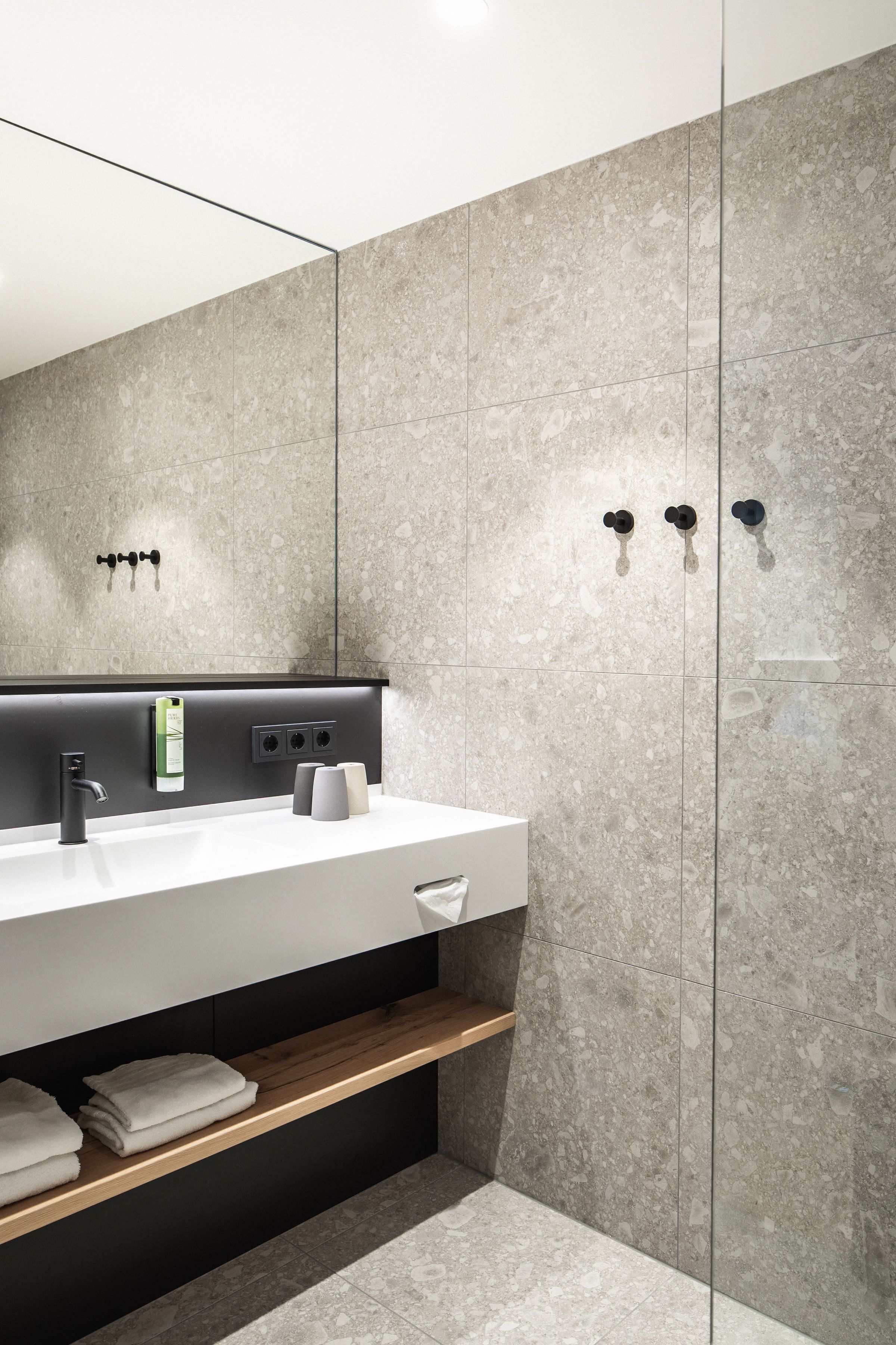 Un baño moderno con un espejo grande, un lavamanos blanco y un estante de madera.
