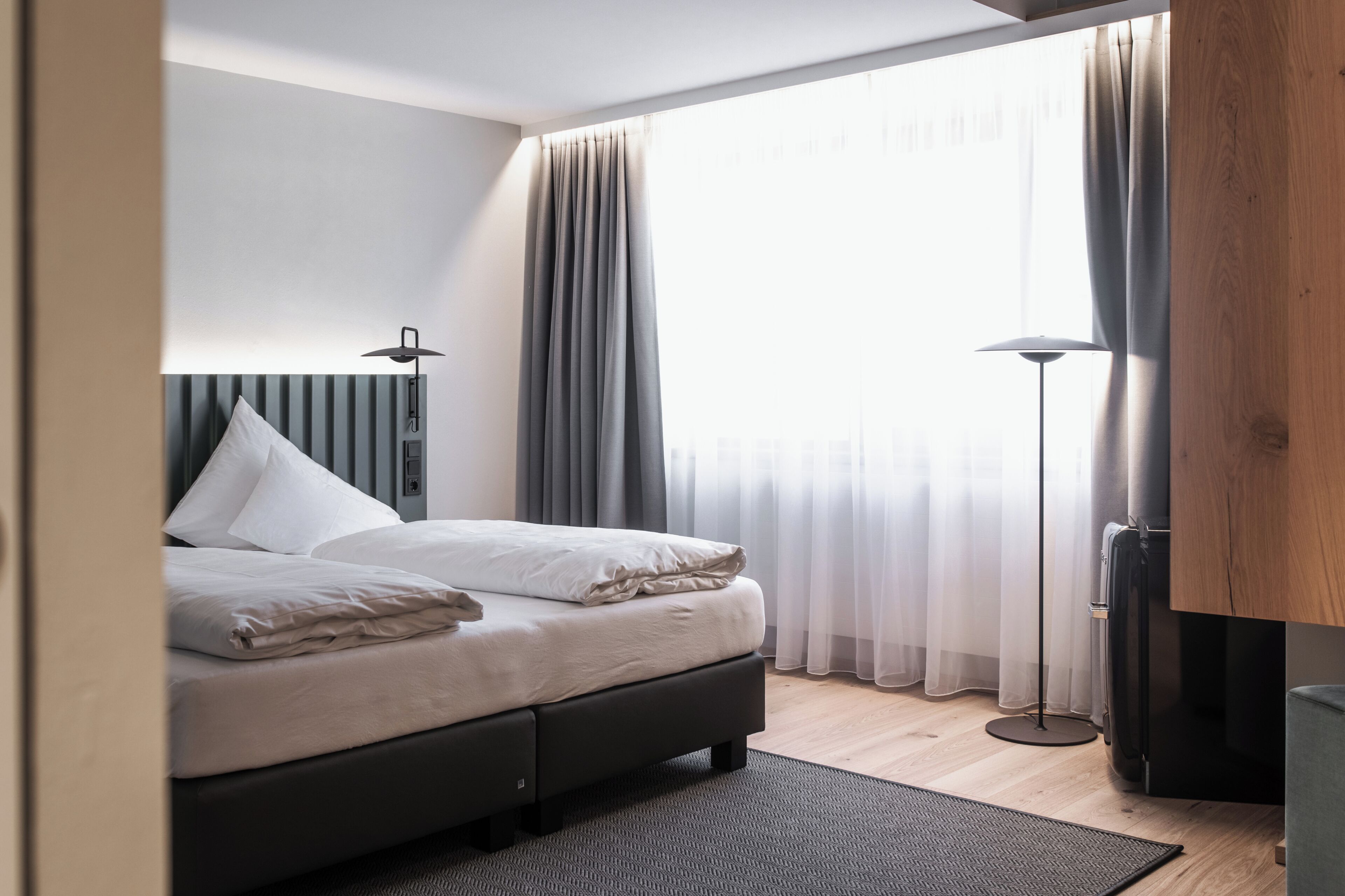 A modern bedroom with a bed, curtains, a floor lamp, and a wooden wardrobe.