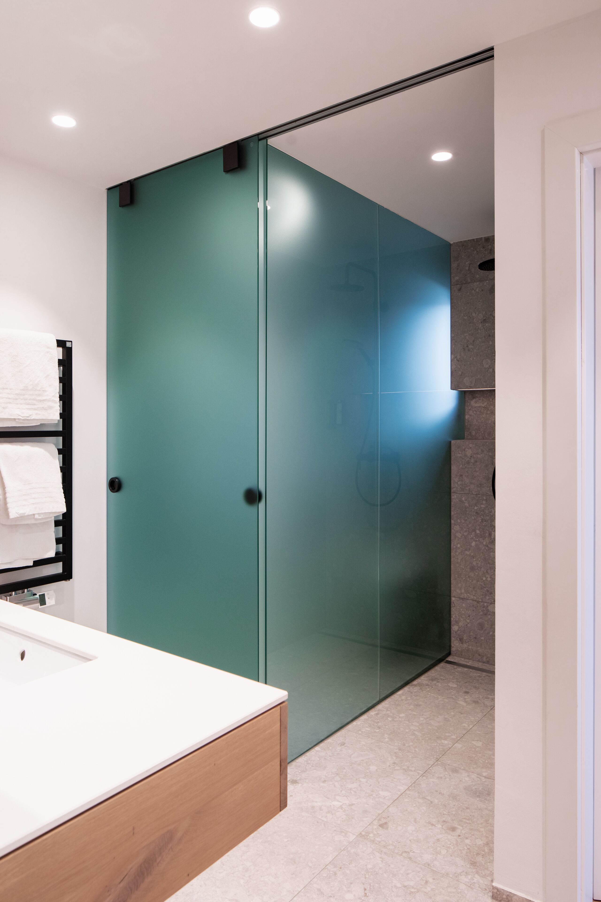 A modern bathroom with a teal shower enclosure, a white sink, and a towel rack.