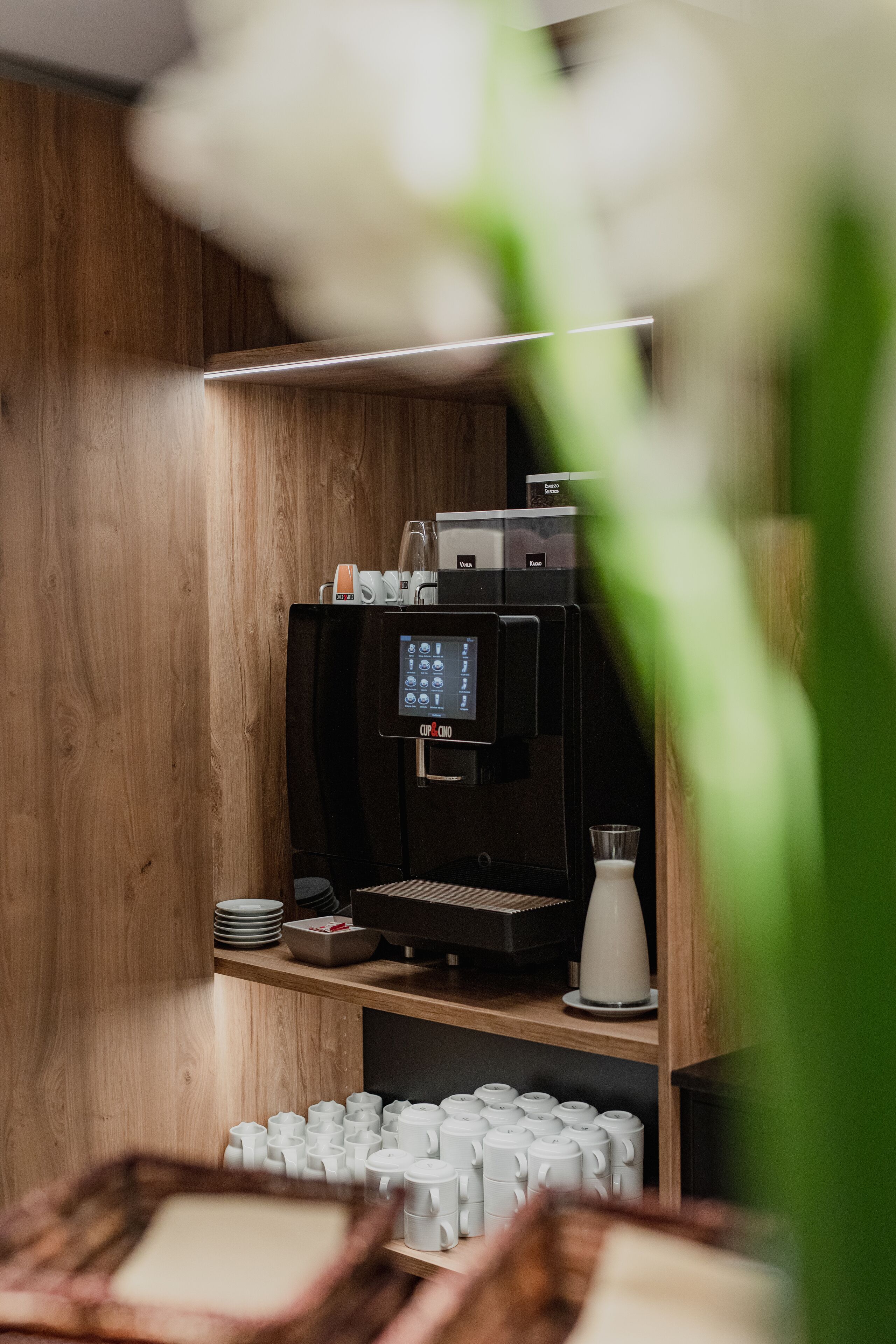 Eine Kaffeemaschine in einem Holzraum mit einem Regal voller Tassen.